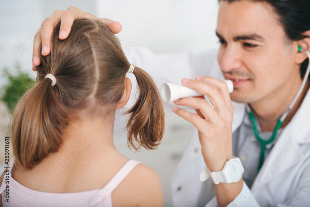 Male doctor examining little girl's ear at hospital, using flashlight Male doctor examining little girl's ear at hospital, using flashlight