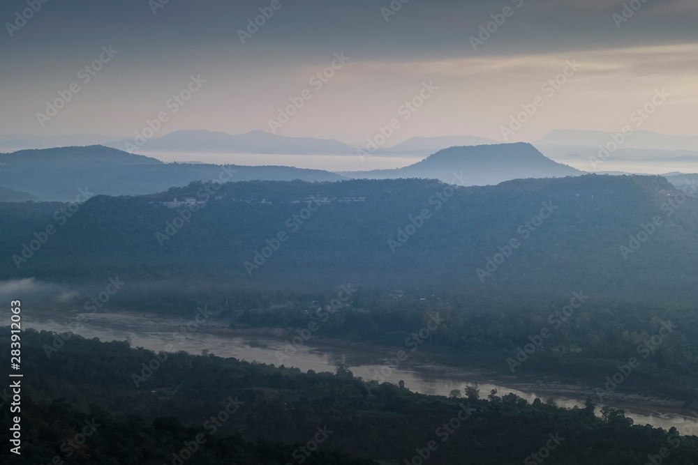 Mountain view morning of Peak mountain above mekong river around with soft mist and cloudy sky background, sunrise at Cha Na Dai Cliff, Pha Taem National Park, Ubon Ratchathani, Thailand.