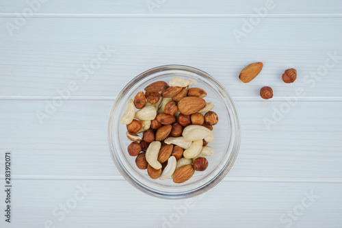 Assorted nuts in a glass bowl on a white wooden background, top view