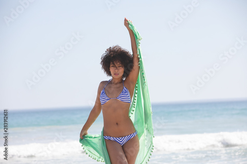 Woman in bikini with scarf standing on the beach