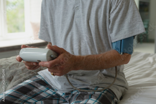 Active senior man measuring blood pressure with sphygmomanometer in bedroom at home