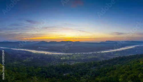 Top view panorama of Mekong river around with soft mist, forest, mountains with cloudy and yellow sun light in the sky background, sunrise at Cha Na Dai Cliff, Ubon Ratchathani, Thailand. © Yuttana Joe