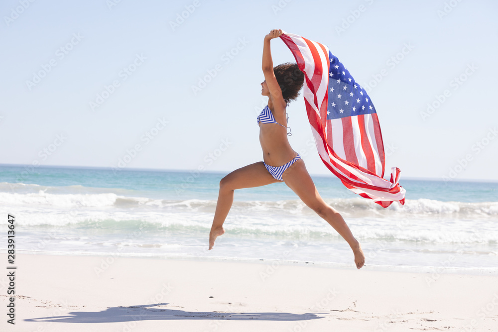 Woman in bikini with american flag jumping on the beach