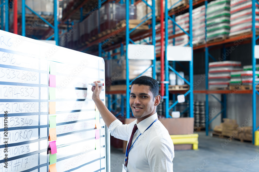 Male supervisor writing on whiteboard in warehouse