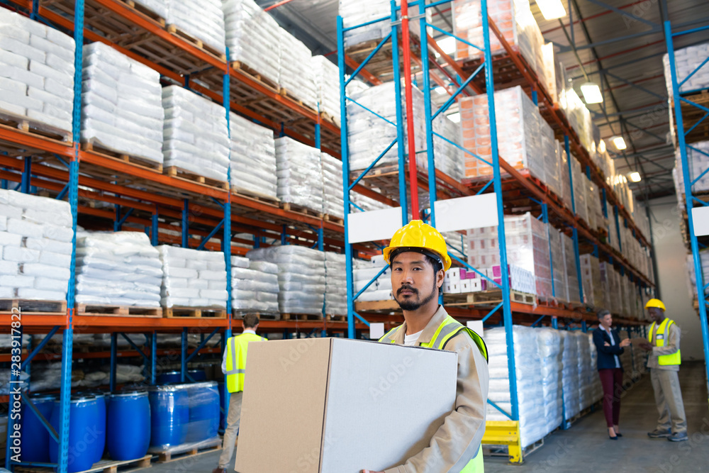 Fototapeta premium Male worker carrying cardboard box and looking at camera in warehouse