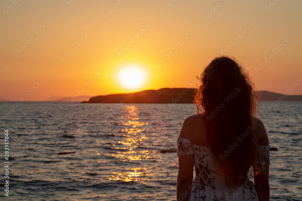 Girl on pontoon pier at sunset . Woman relaxing on pier looking at sea view at sunset