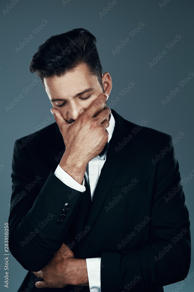 Tired young man in bow tie covering mouth with hand while standing against grey background Tired young man in bow tie covering mouth with hand while standing against grey background