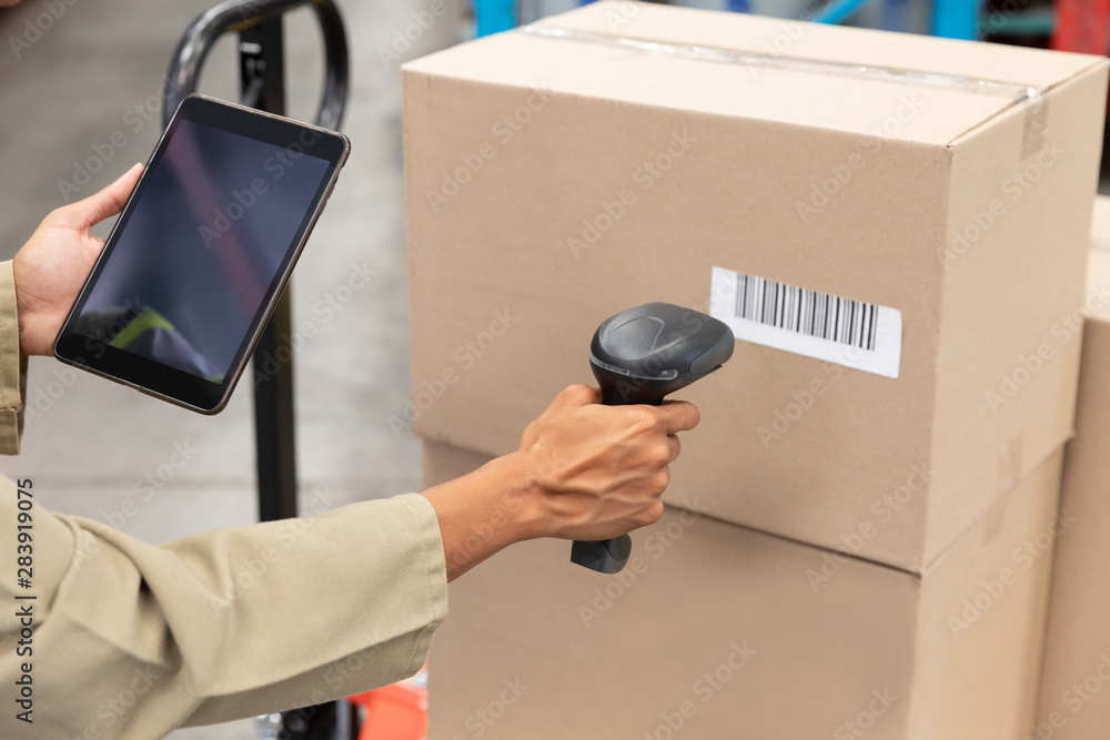 Female worker scanning package with barcode scanner while using digital tablet in warehouse - obrazy, fototapety, plakaty 