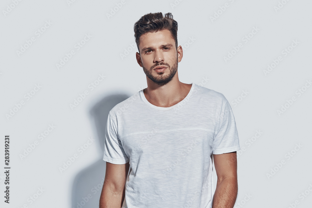 Handsome young man looking at camera while standing against grey background Handsome young man looking at camera while standing against grey background
