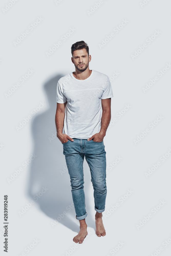 Full length of handsome young man looking at camera while standing against grey background Full length of handsome young man looking at camera while standing against grey background