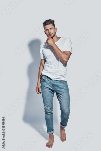 Full length of handsome young man looking at camera while standing against grey background