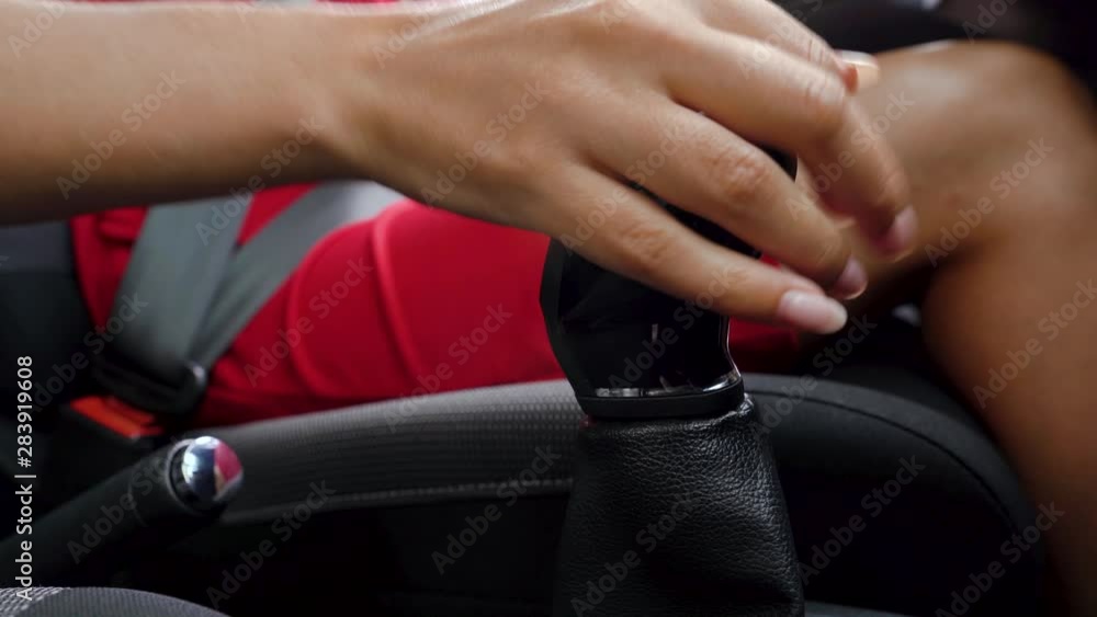 Close-up of woman driver in a red dress fastens her seat belt, changes gear and starts moving Close-up of woman driver in a red dress fastens her seat belt, changes gear and starts moving