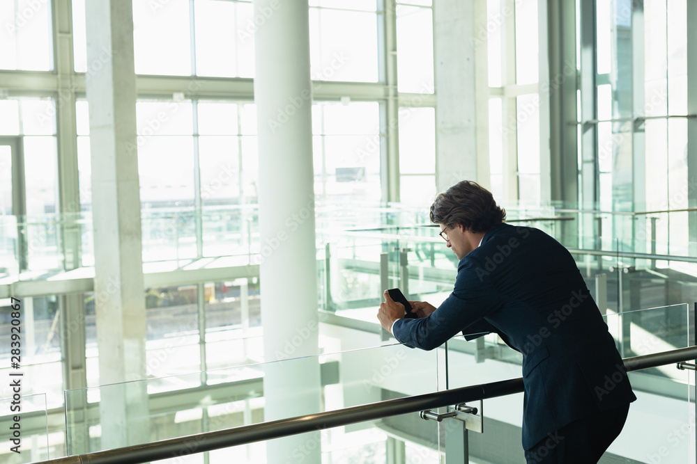Businessman leaning on railing and using mobile phone in a modern office building Businessman leaning on railing and using mobile phone in a modern office building