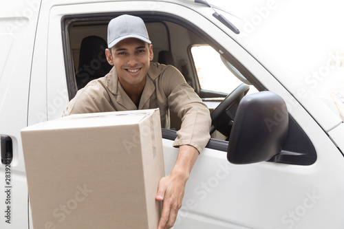 Delivery man holding a package while sitting in van outside the warehouse