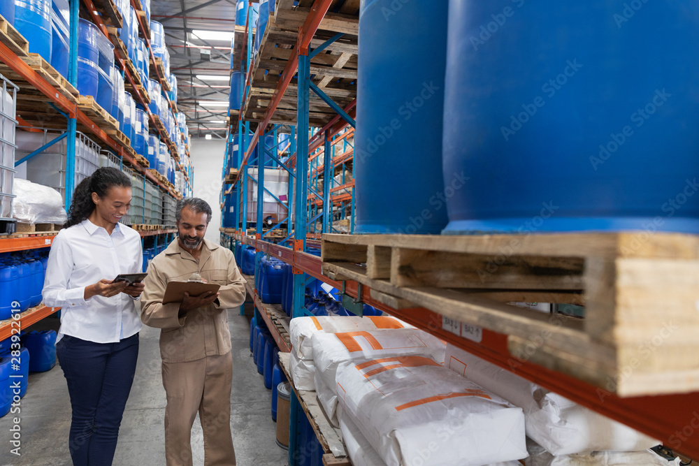 Female manager and male staff discussing over clipboard in warehouse Female manager and male staff discussing over clipboard in warehouse