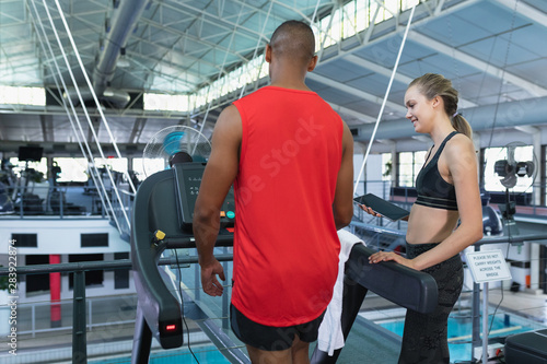Female trainer assisting man to work out on treadmill