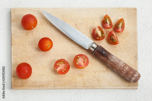Horizontal photo of a wooden cutting board with knife and cut red cherry tomatoes, preparing healthy food for cooking. 
