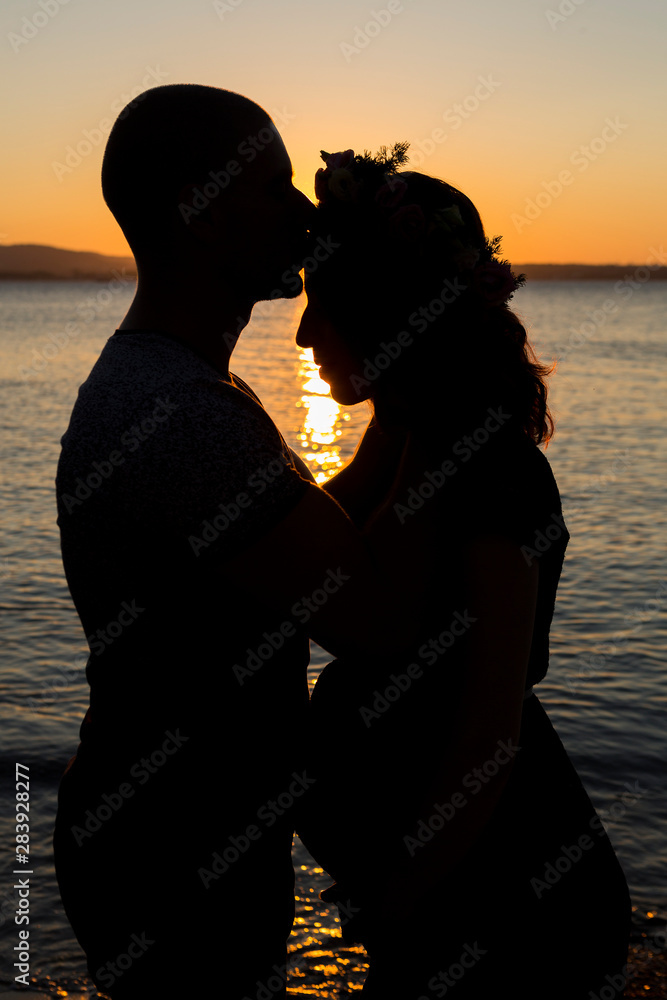 pregnant couple on the beach at sunset. pregnant girl posing with her husband against the background of a beautiful sunset during the blue hour.  waiting for the baby.