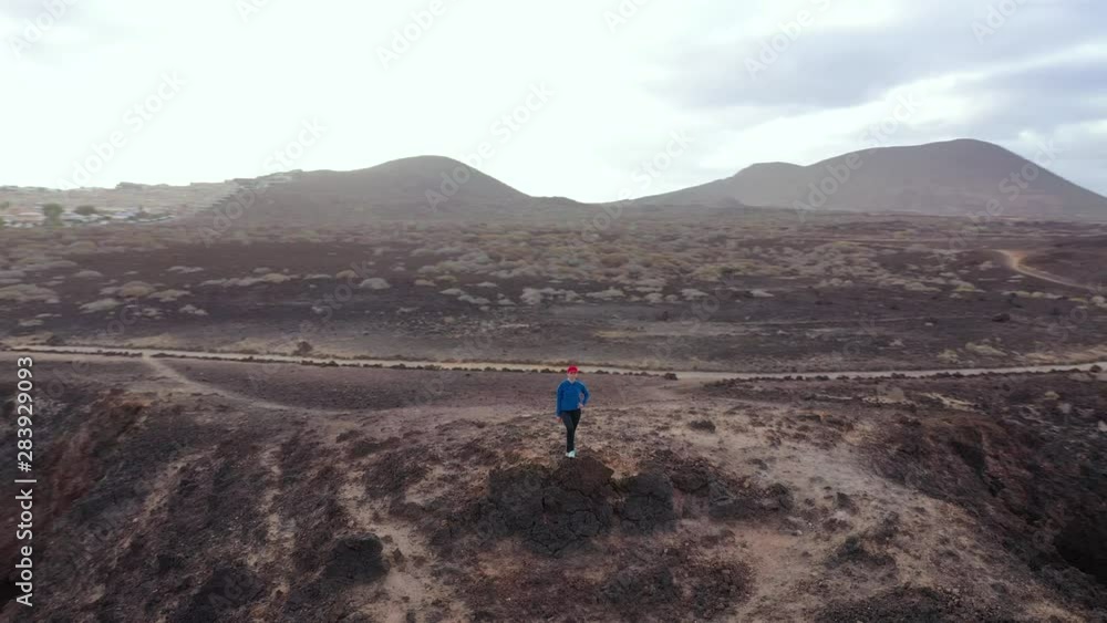 Aerial view of woman in sportswear after jogging stands on top of a rock and enjoys the scenery in a conservation area on the shores of the Atlantic Ocean. Tenerife, Canary Islands, Spain Aerial view of woman in sportswear after jogging stands on top of a rock and enjoys the scenery in a conservation area on the shores of the Atlantic Ocean. Tenerife, Canary Islands, Spain