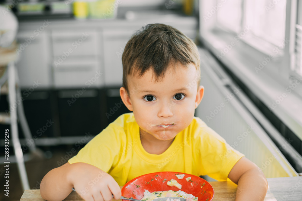 Φωτογραφία A child in a yellow t-shirt in the kitchen eating Russian national dish Okroshka