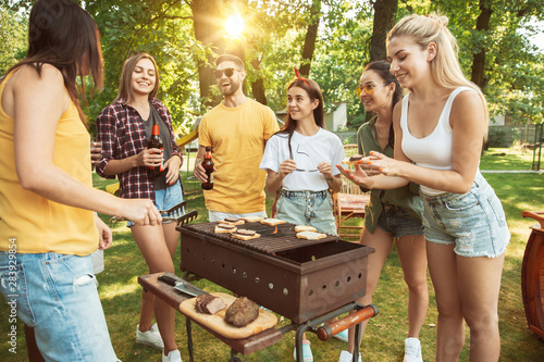 Group of happy friends having beer and barbecue party at sunny day. Resting together outdoor in a forest glade or backyard. Celebrating and relaxing, laughting. Summer lifestyle, friendship concept.