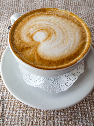 Hot cappuccino with froth and pattern on ackcloth background, a side view