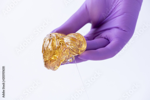 Woman's hand in a glove holds yellow sugar paste or wax for depilation close up on a white background