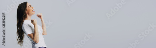 side view of excited happy beautiful girl in white t-shirt showing yes gesture isolated on grey, panoramic shot