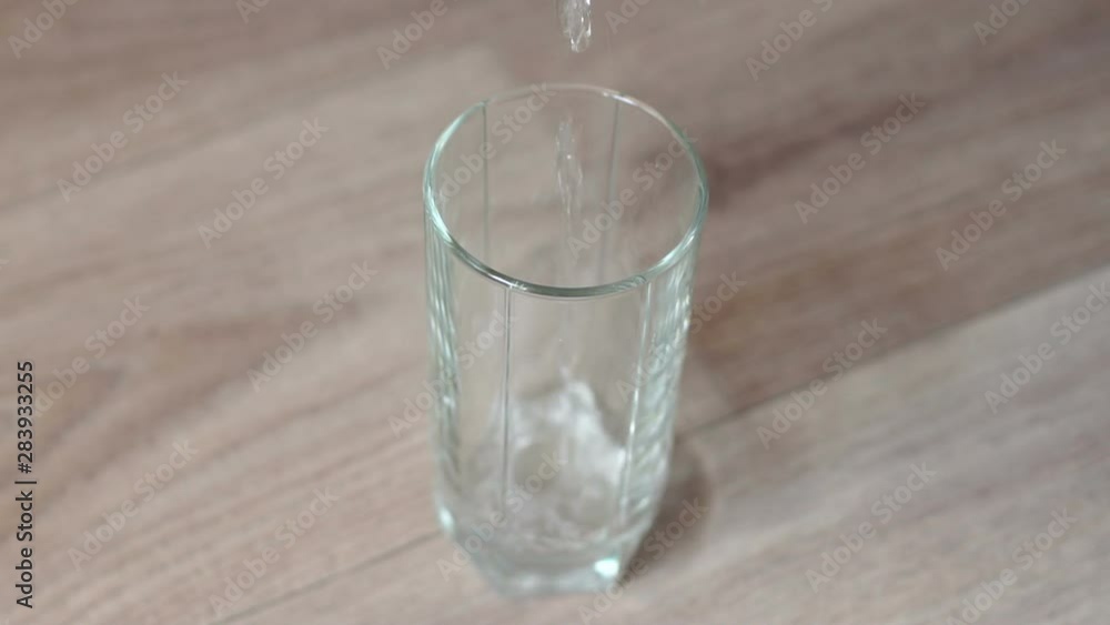 Close-up of a woman pouring water into a glass on a wooden table. Slow motion. Clean water in a glass on a wooden table. Close-up of a woman pouring water into a glass on a wooden table. Slow motion. Clean water in a glass on a wooden table.