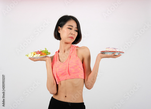 sporty fitness woman in sportswear with vegetable salad & cake on white background. healthy sport