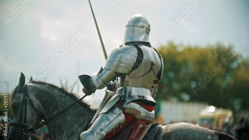 A man knight riding a horse around the battlefield and greeting the people watching behind the fence - raises his hand up in the sky holding a sword photo