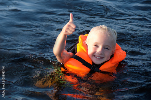 Happy blond little girl swimming in orange life jacket in the sea. girl shows thumb up