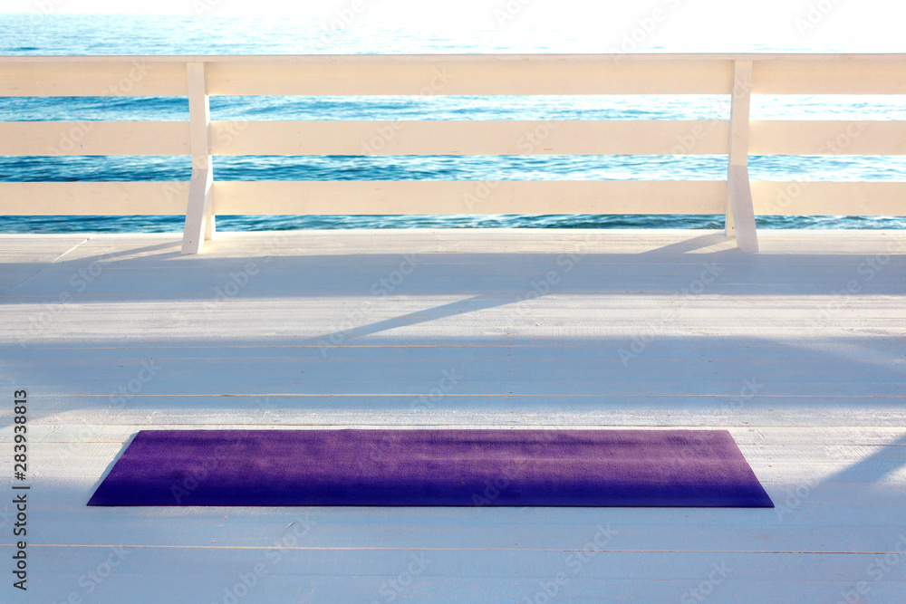 Violet yoga mat lying on white wooden seafront. Minimalistic sport background with copy space