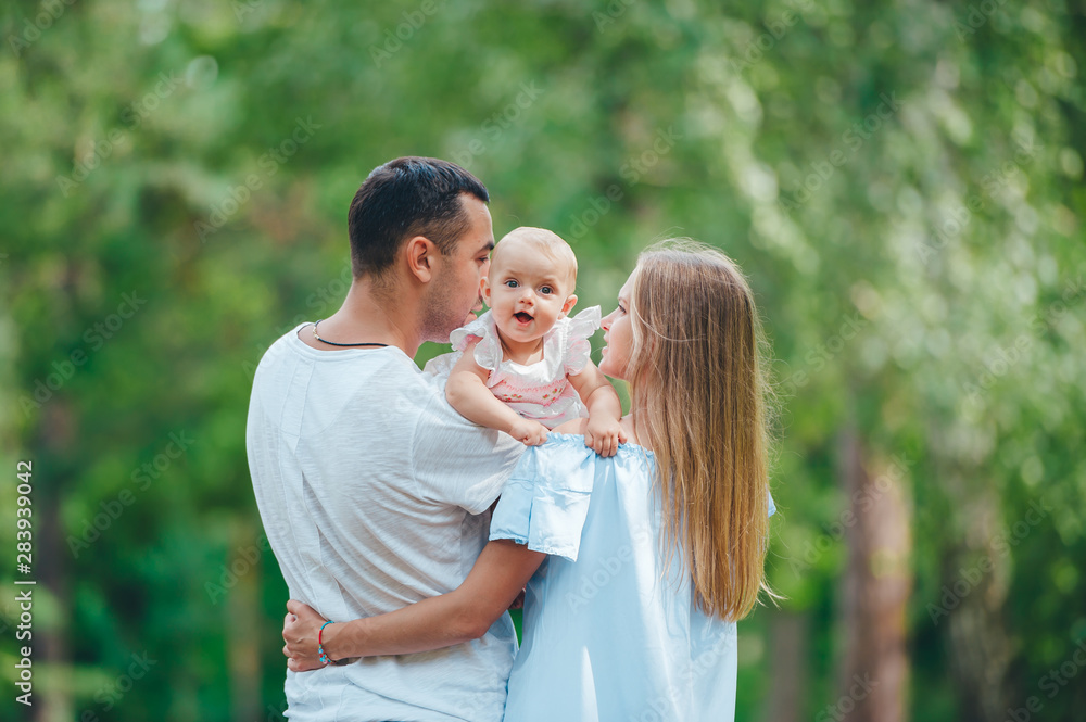 Young beautiful woman, handsome man and small cute daughter outdoors. Blurred green background Young beautiful woman, handsome man and small cute daughter outdoors. Blurred green background