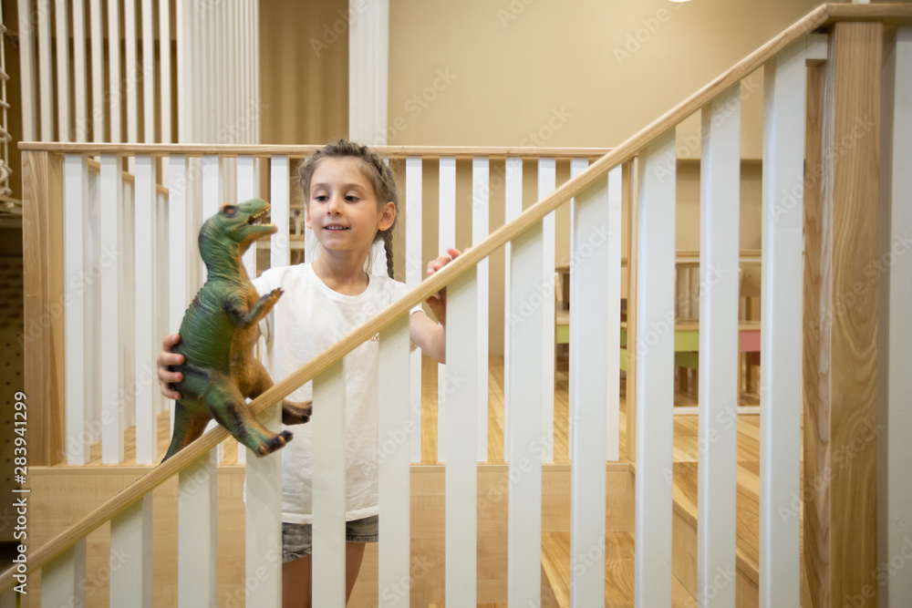 Girl kid playing with a toy dinosaur on wooden stairway