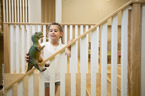 Girl kid playing with a toy dinosaur on wooden stairway © 4Max