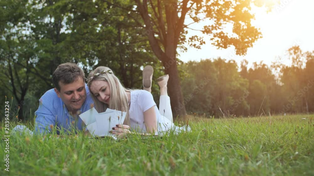 A guy and a girl are watching a family album with photos in the park on the grass. A guy and a girl are watching a family album with photos in the park on the grass.