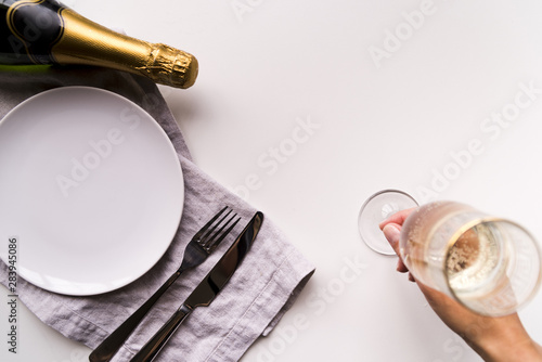 Overhead view of human hand putting champagne glass near empty white plate on plain background