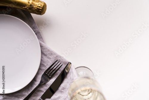 Champagne bottle and glass with empty plate on white backdrop