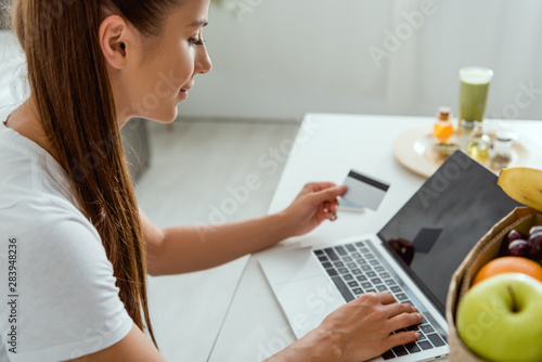 selective focus of happy girl holding credit card near laptop