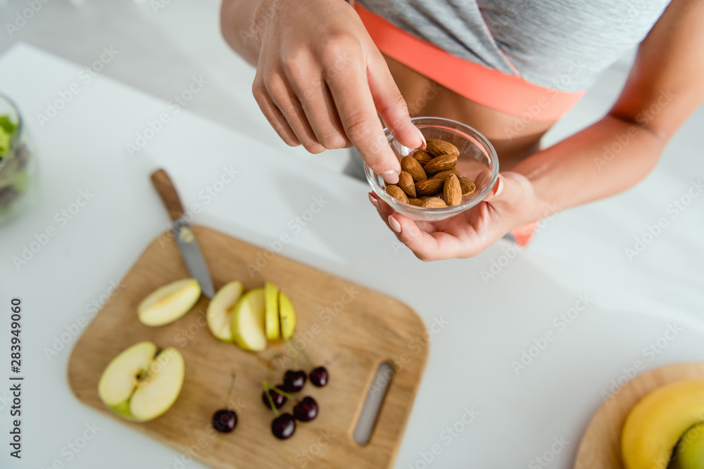 overhead view of girl holding bowl with almonds near cutting board with fruits