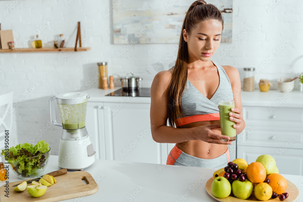 selective focus of attractive girl with sportswear holding glass with tasty smoothie