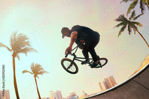 Photo BMX rider is performing tricks in skatepark on sunset.