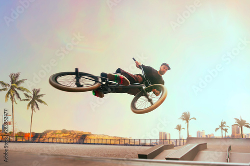 Fototapeta BMX rider is performing tricks in skatepark on sunset.