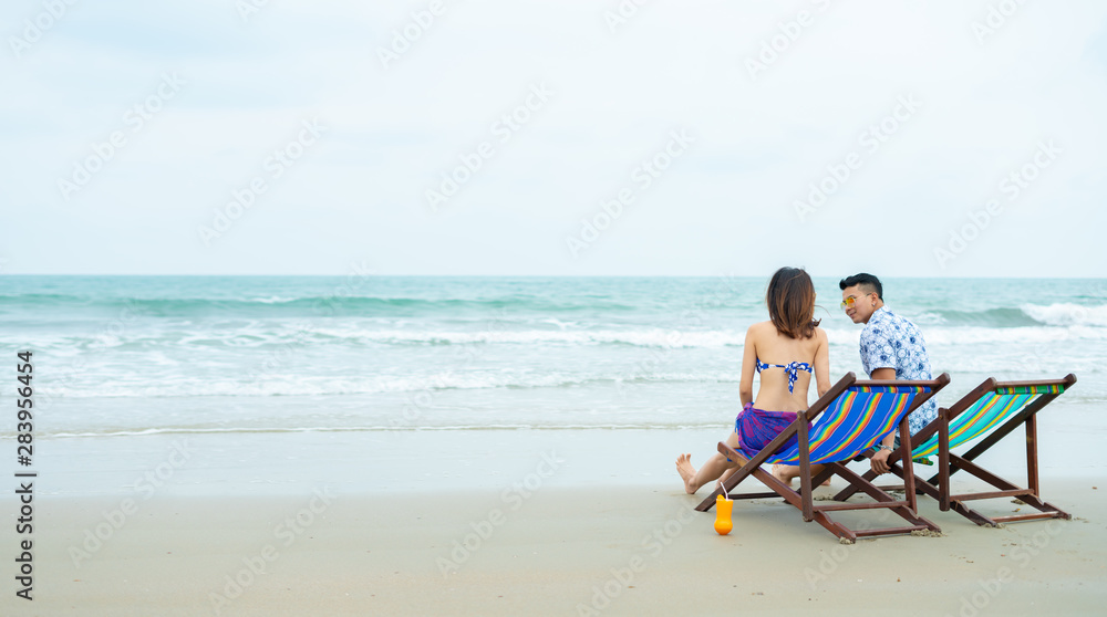 Young Asian honeymoon couple in holiday beach and sitting on beach. Asian couple in bikini walking on thailand beach romantic travel honeymoon vacation summer holiday romance.