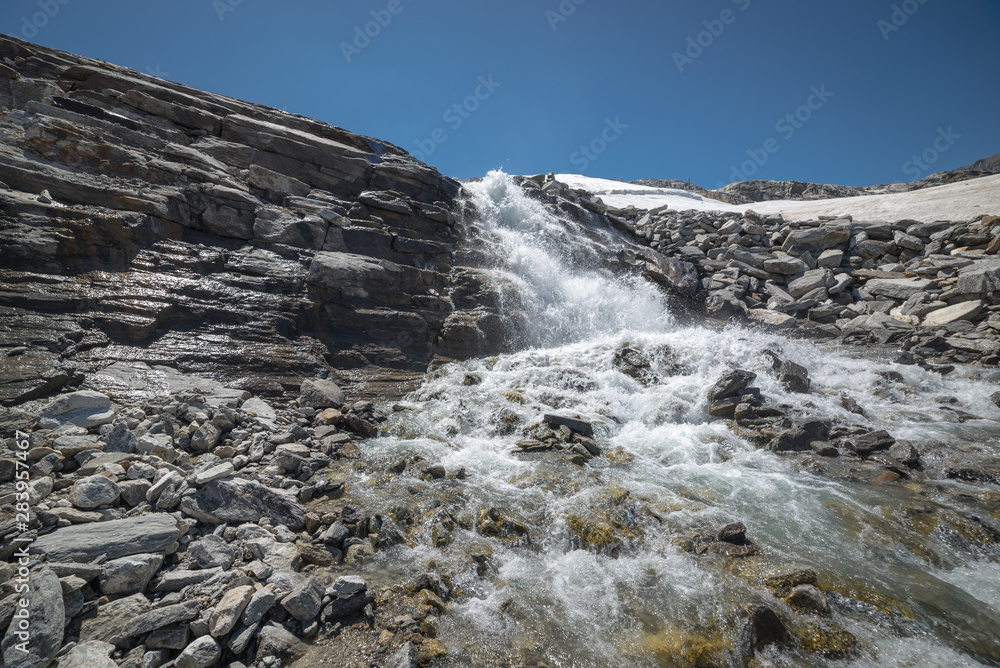 Waterfall and stream in a rocky and snowy alpine landscape