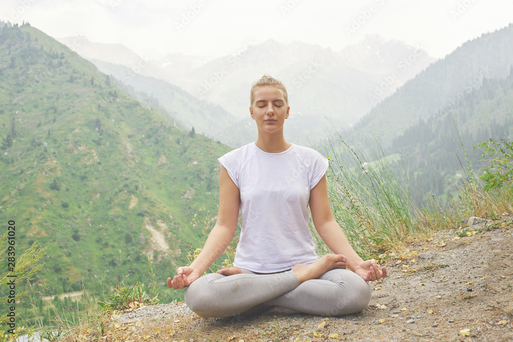 Sport girl doing yoga in mountains beautiful landscape. Young woman leads healthy lifestyle, meditates, relaxes lotus position in bright sportswear on nature