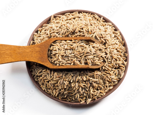 Cumin seeds (Cuminum), jeera in a wooden scoop on a clay plate on a white background