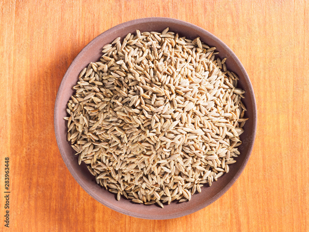 Cumin seeds (Cuminum), Jeera in a clay plate on a brown wood background Cumin seeds (Cuminum), Jeera in a clay plate on a brown wood background