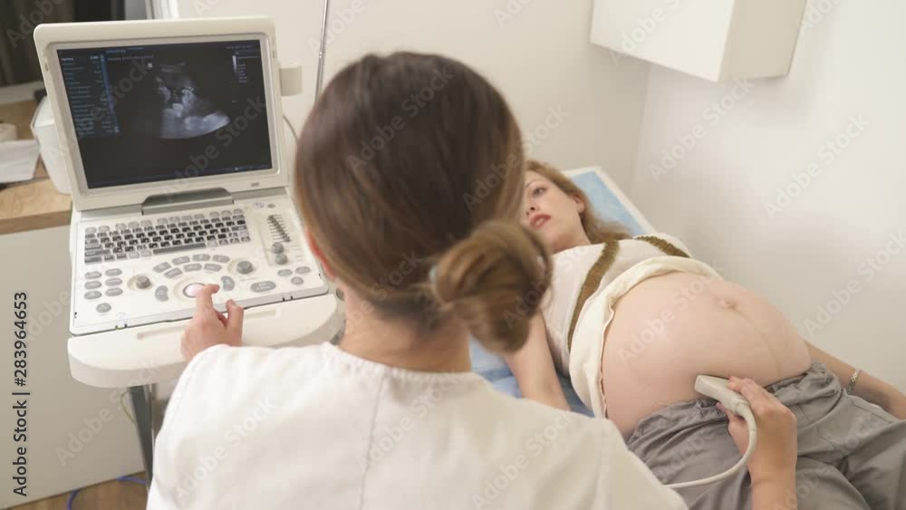 Doctor communicating with her pregnant patient while doing ultra sound check-up. Medical examining by ultrasonic scan. High angle view Doctor communicating with her pregnant patient while doing ultra sound check-up. Medical examining by ultrasonic scan. High angle view